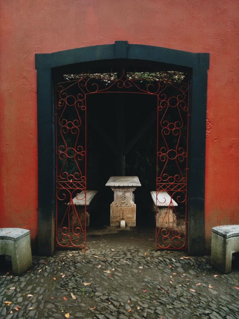 A photograph of an open entryway to a passage with seating. The walls around the doorway are red, as is the metalwork around the archway.